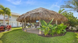 A thatched gazebo in a well-maintained garden with a pool table and chairs. - The Kove  (Fort Myers Beach)