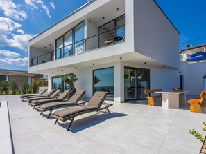 Un edificio moderno de dos pisos con un área de piscina en la azotea, que incluye sillones de sol y una mesa.