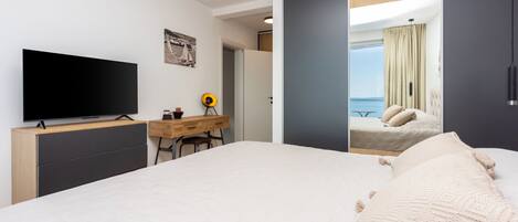 A hotel room with a bed, a desk, a television, and a view of the sea.