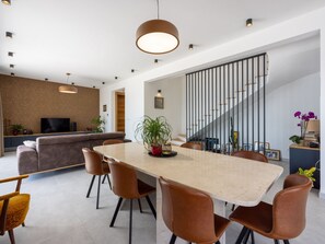Una cocina moderna con televisor de pantalla plana, un comedor con mesa y sillas grandes, y una escalera con barandilla.