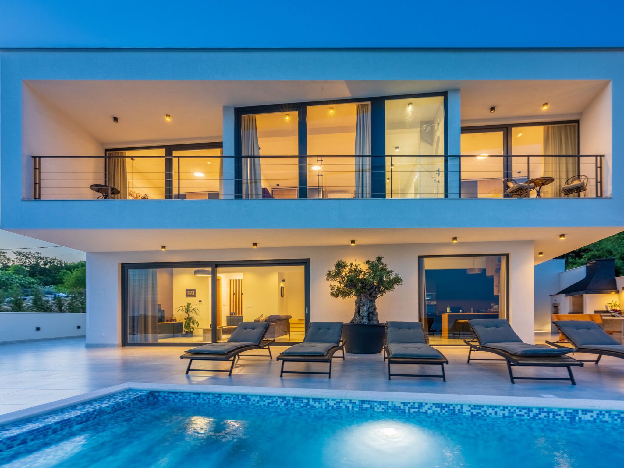 A modern two-story house with a swimming pool, lounge chairs, and a large potted plant.