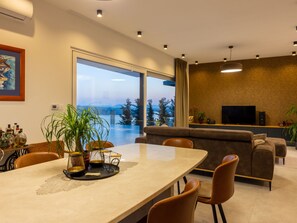 A modern living room with a large window, a dining area with a table and chairs, a sofa, and a television. - Villa Murn / HR-11124-01 by Interhome (Crikvenica)