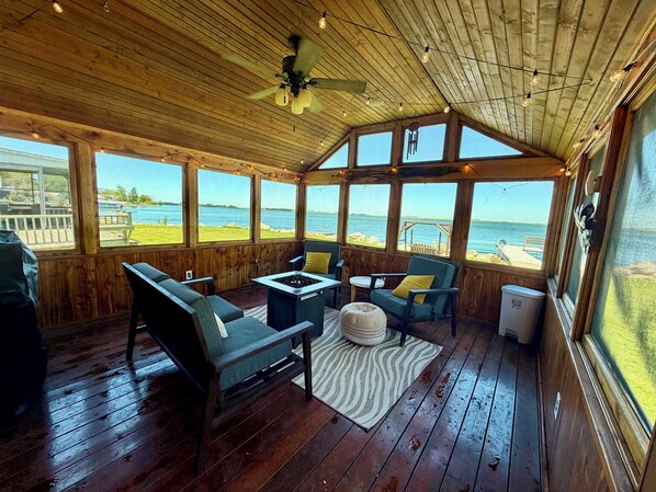 Een houten terras met een plafondventilator, een tafel met stoelen en uitzicht op het water.