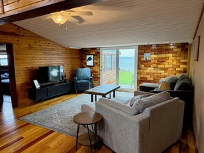 A cozy cabin interior with wooden walls, a television, a sofa, and a table. - Relaxing 3BR Cabin on Blue Dog Lake I Screened Porch I Fireplace I Lakefront (Waubay)