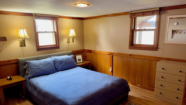 A bedroom with a bed, two bedside lamps, a dresser, and a window. - Relaxing 3BR Cabin on Blue Dog Lake I Screened Porch I Fireplace I Lakefront (Waubay)