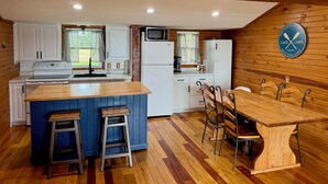 A cabin interior with a kitchen, dining area, and a logo on the wall. - Relaxing 3BR Cabin on Blue Dog Lake I Screened Porch I Fireplace I Lakefront (Waubay)