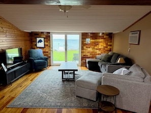 A living room with a television, seating, a coffee table, and a view through a glass door. - Relaxing 3BR Cabin on Blue Dog Lake I Screened Porch I Fireplace I Lakefront (Waubay)