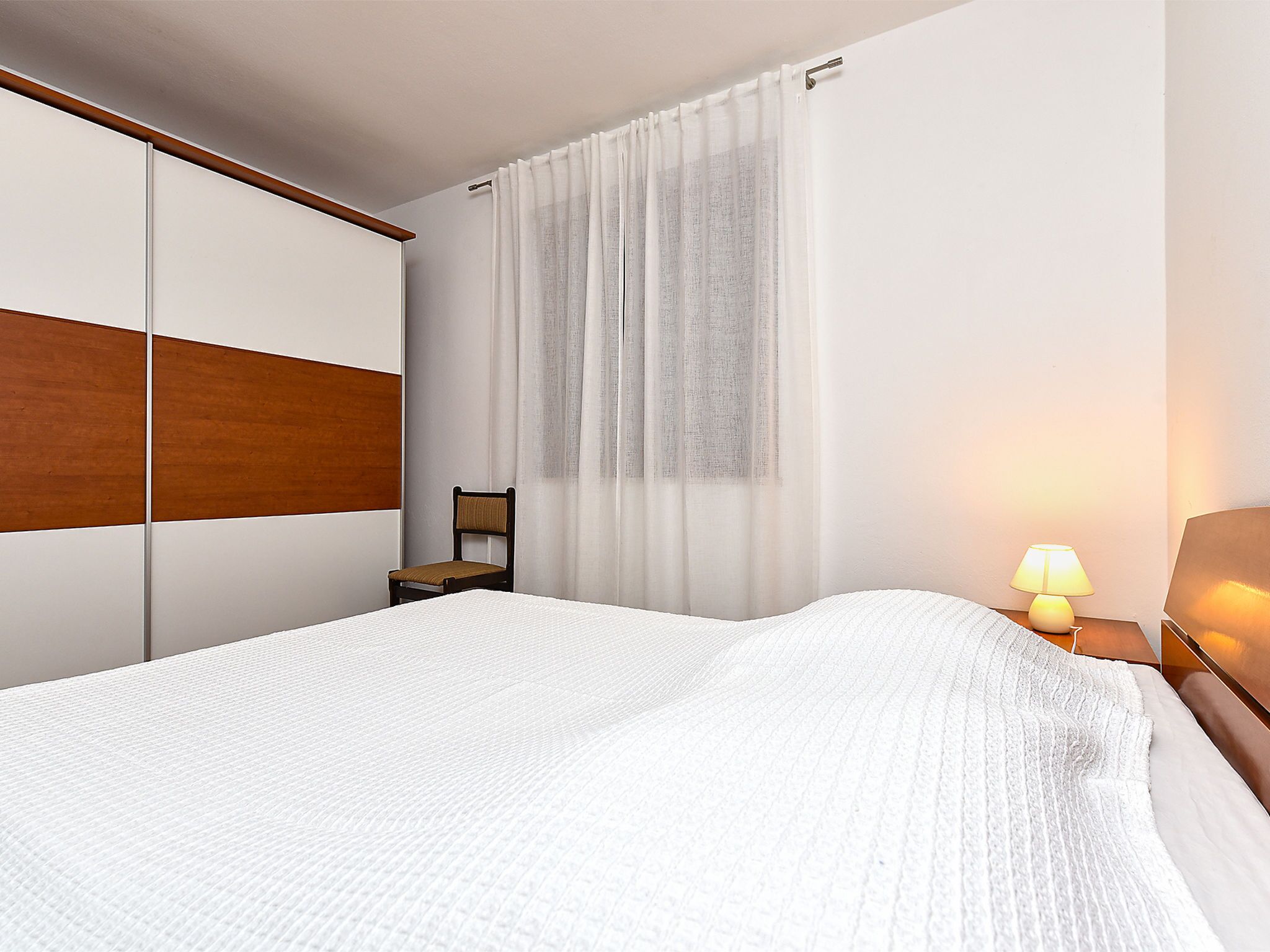 A hotel room with a bed, a chair, a nightstand, a lamp, and a window with curtains.