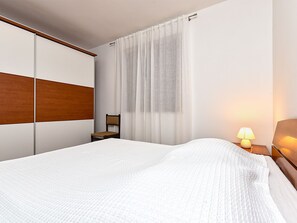 Una habitación de hotel con cama, una silla, una mesita de noche, una lámpara y una ventana con cortinas.
