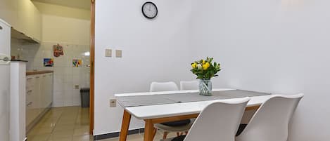 Une cuisine de taille réduite avec un coin repas, une horloge au mur et un vase rempli de fleurs sur la table.