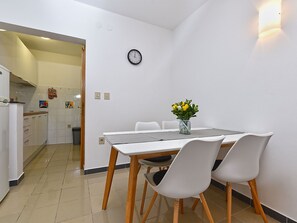 A compact kitchen with a dining area, a clock on the wall, and a vase with flowers on the table. - Apartment 2372 by Interhome (Drenje)