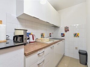 A kitchen with white cabinets, a wooden countertop, a coffee maker, a kettle, and colorful tiles on the backsplash. - Apartment 2372 by Interhome (Drenje)