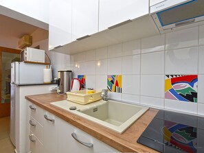 A kitchen with white cabinets, a wooden countertop, a sink, a coffee maker, and colorful tiles on the backsplash. - Apartment 2372 by Interhome (Drenje)