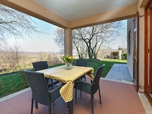 A covered patio with a table set for two, surrounded by chairs, overlooking a landscaped garden and a distant view. - Apartment 2372 by Interhome (Drenje)