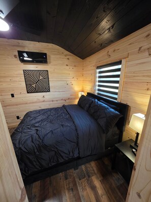 A bedroom with a bed, a nightstand, a wall-mounted heater, and a window with blinds. - Sweet Alfalfa 185 Texas USA (Van Zandt County)