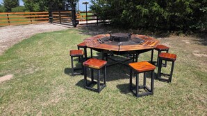 Een houten tafel buiten met vier stoelen, omringd door gras en bomen.