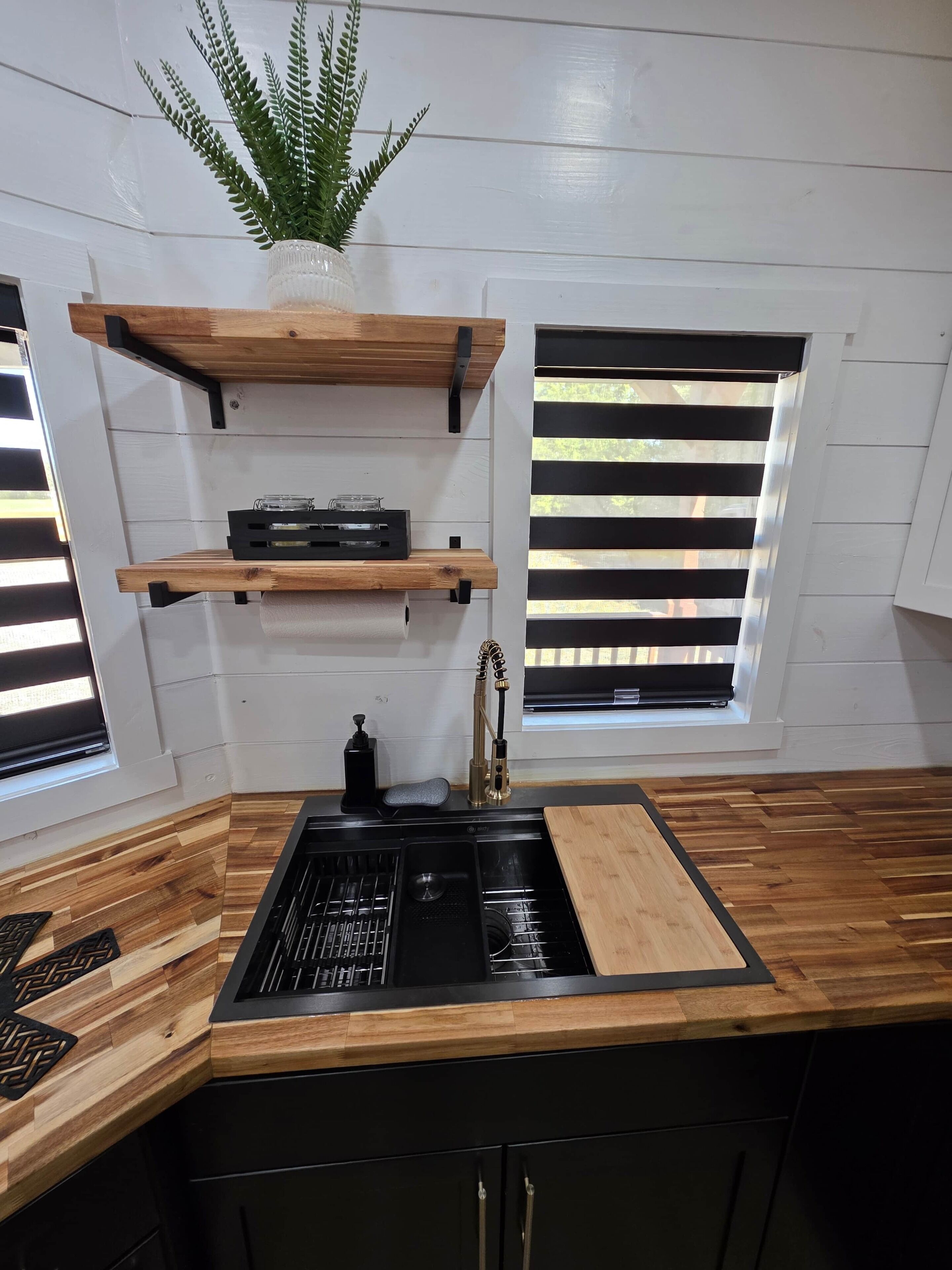 Eine Küche mit einem schwarzen Spülbecken, Holz Arbeitsplatten und einer Topfpflanze auf einem Regal.