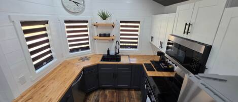 A compact kitchen with a wooden countertop, black cabinets, a stainless steel stove, and a clock on the wall.
