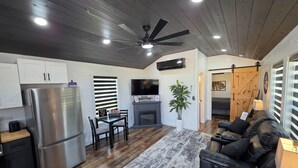 Una cocina moderna con un refrigerador de acero inoxidable, una zona de comedor con una mesa y sillas, un ventilador de techo y un televisor de pantalla plana grande.