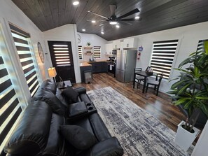 A modern kitchen with a central island, a dining area with a table and chairs, and a living room with a black leather sofa. - Hay Meadow 189 Texas USA (Van Zandt County)
