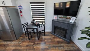 Una cocina compacta con refrigerador, una mesa de comedor con sillas, una chimenea y un televisor montado sobre ella.