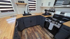 Una cocina moderna con gabinetes oscuros, encimera de madera, barra de café y horno de acero inoxidable.