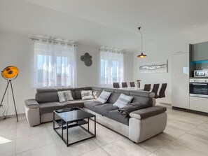 A modern living room with a sectional sofa, a glass coffee table, and a kitchen area with appliances. - Apartment 2217 by Interhome (Medulin)