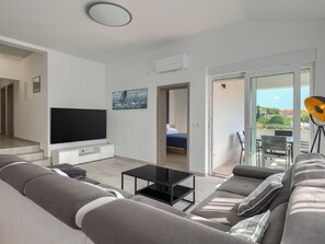 A modern living room with a flat-screen TV, a sofa, a coffee table, and a balcony with a table and chairs. - Apartment 2217 by Interhome (Medulin)