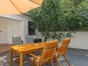 Eine Terrasse im Freien mit Holztisch und -stühlen, einem überdachten Sitzbereich und einem Baum, der Schatten spendet.