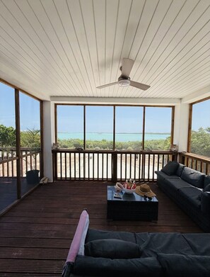 A sunlit room with a ceiling fan, large windows, a wooden deck, and a sofa.