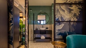 Een moderne badkamer met spiegel, wastafel en een blauwgroene stoel.