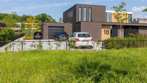 Een modern gebouw met een garage, een garagepoort met nummer 16, en een parkeerplaats met twee auto's.