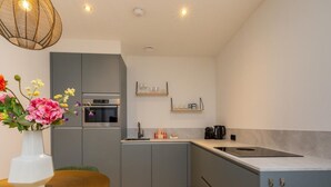 Een moderne keuken met grijze kastjes, een inbouwoven en een eethoek met een tafel en stoelen.