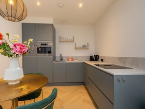 A modern kitchen with grey cabinets, a built-in oven, and a dining area with a table and chairs. - RustUit by Interhome (Koudekerke)