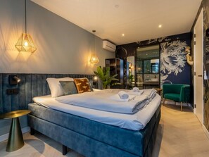 A modern bedroom with a large bed, bedside lamps, a green chair, and a decorative wall mural. - RustUit by Interhome (Koudekerke)