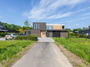 A modern building with a flat roof, large windows, and a paved driveway leading to the entrance. - RustUit by Interhome (Koudekerke)