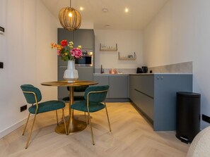 A modern kitchen with a round table and chairs, a vase of flowers, and a coffee machine. - RustUit by Interhome (Koudekerke)