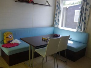 A room with a blue sofa, a small table, and a chair. There is a yellow backpack and a red cloth on the sofa. - Mobile home for 4 people with terrace (Martiel)