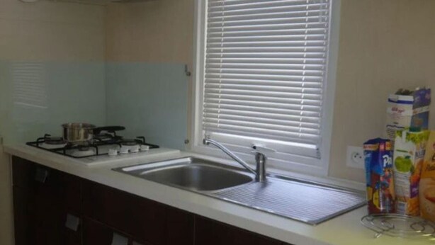 A kitchen with a gas stove, a sink, and a window with blinds. - Mobile home for 4 people with terrace (Martiel)