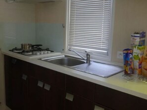 A kitchen with a gas stove, a sink, and a window with blinds. - Mobile home for 4 people with terrace (Martiel)