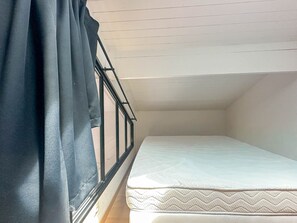 A small, single-bed room with a sloped ceiling and a window with black curtains.
