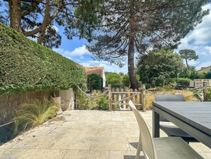 A paved outdoor area with a wooden gate, a picnic table, and a hedge.