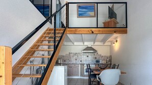 Een moderne keuken met een eetgedeelte, een trap met houten leuningen en uitzicht op zee door een raam.