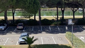 Ein Parkplatz mit mehreren Stellplätzen, dahinter ein Gewässer und Bäume rundherum.