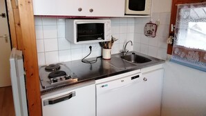 Eine kleine Küche mit weißen Schränken, einer Mikrowelle, einem Spülbecken und einem Herd.