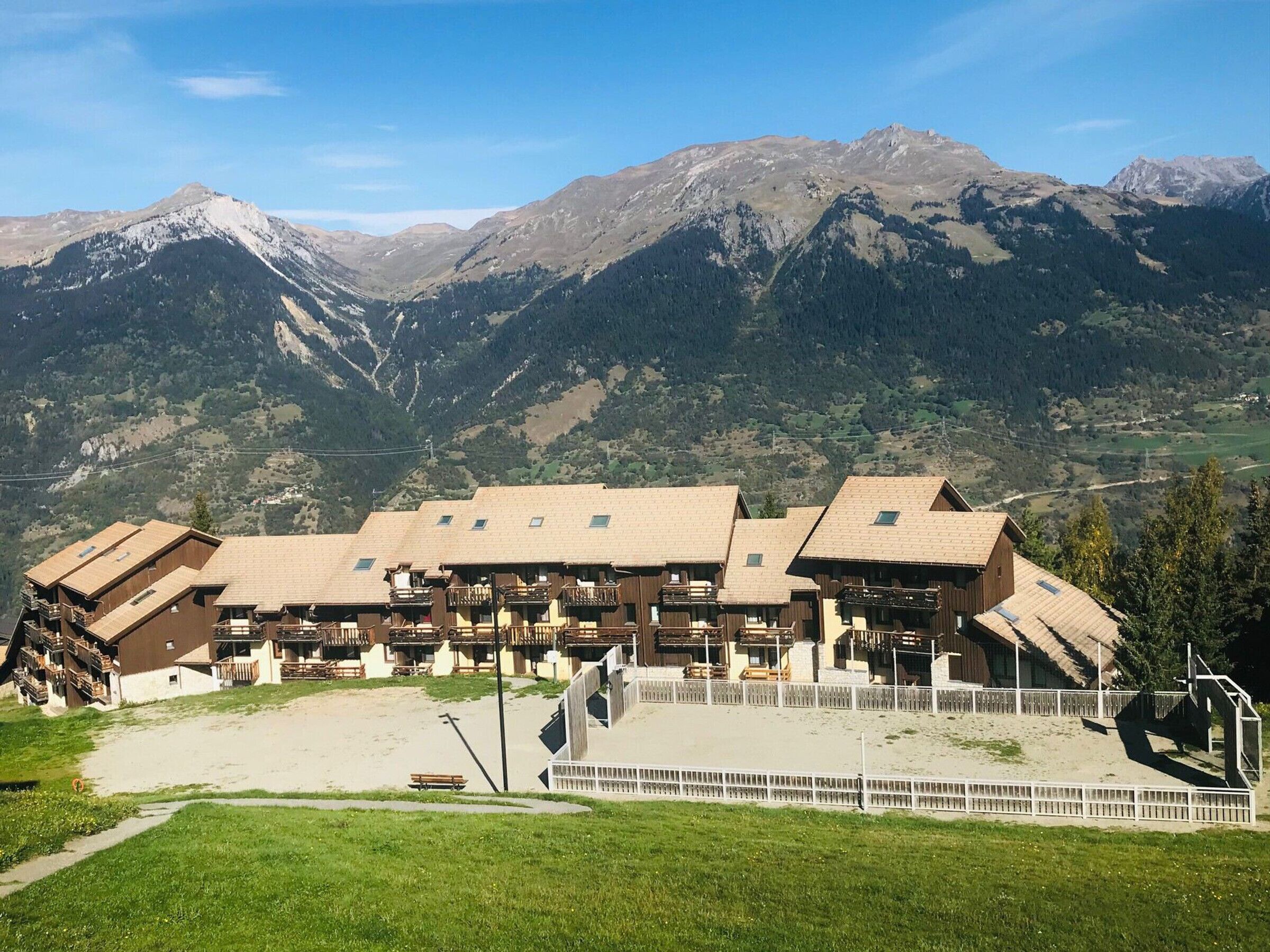 A chalet-style hotel with multiple wooden buildings, a central courtyard, and a mountain backdrop.