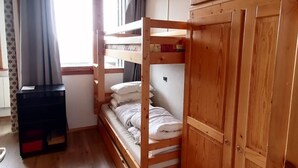 Ein Schlafraum mit Etagenbetten, einem Kleiderschrank, einem kleinen Tisch und einem Fenster mit Vorhängen.