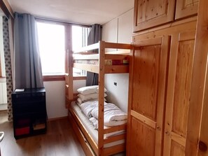 Ett rum med en våningssäng, en garderob, ett litet bord och ett fönster med gardiner.