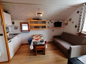 Ett kompakt bostadsutrymme med ett litet kök, ett matbord, en soffa och en TV.