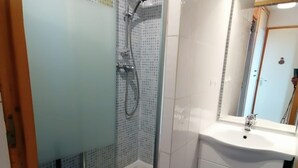 Ein Badezimmer mit einer Duschkabine, einem weißen Waschbecken und einem Spiegel.